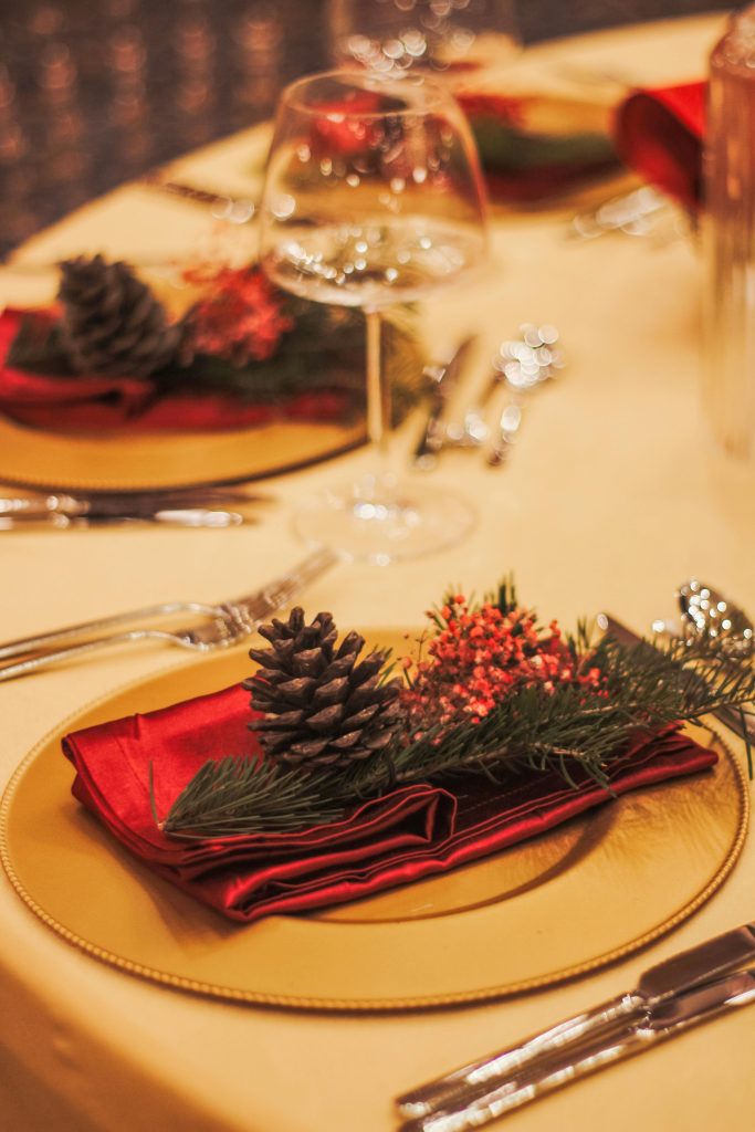 Festive Christmas table setting with pine cones, red napkins, and elegant glassware.